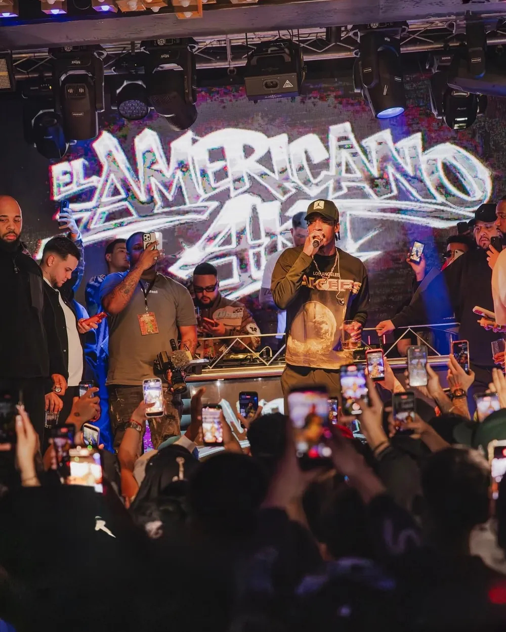 El Americano 4KT cantando en directo, con su nombre en la pantalla y el público grabando con el móvil