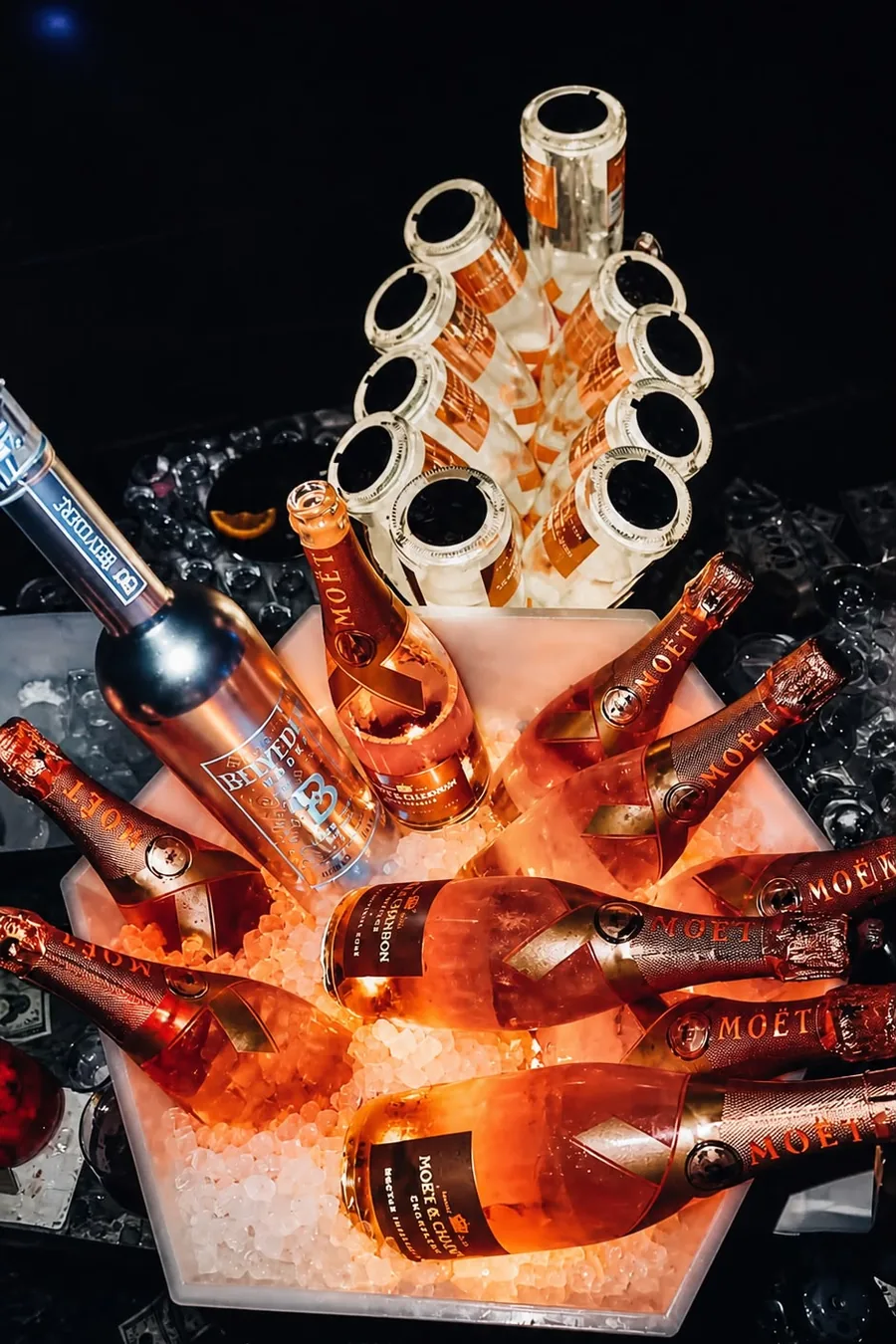 Botellas de champán rosado y vodka sobre hielo iluminado en una mesa reservada